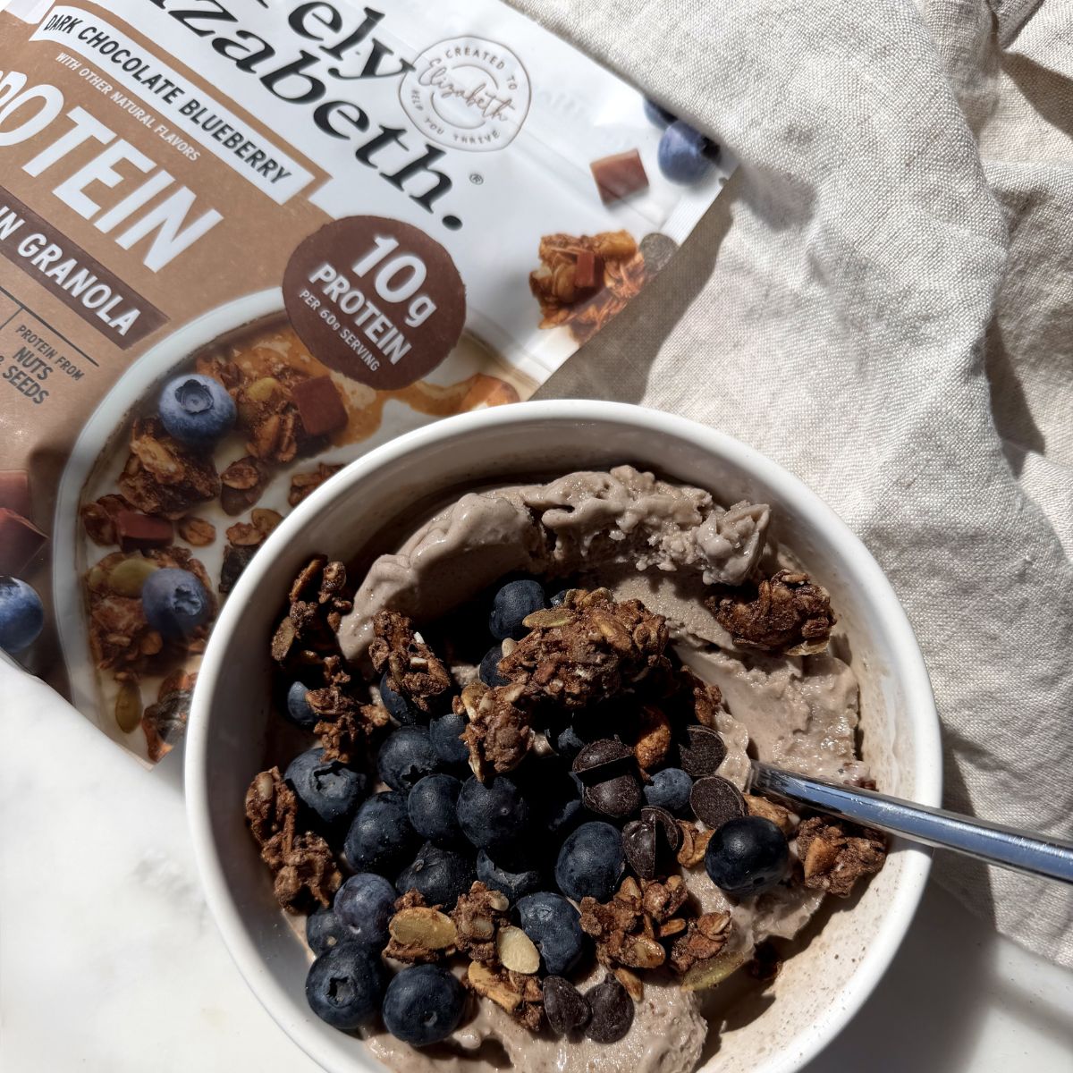 Creamy chocolate smoothie bowl topped with blueberries, mini chocolate chips, and crunchy Purely Elizabeth Dark Chocolate Blueberry Protein Granola.