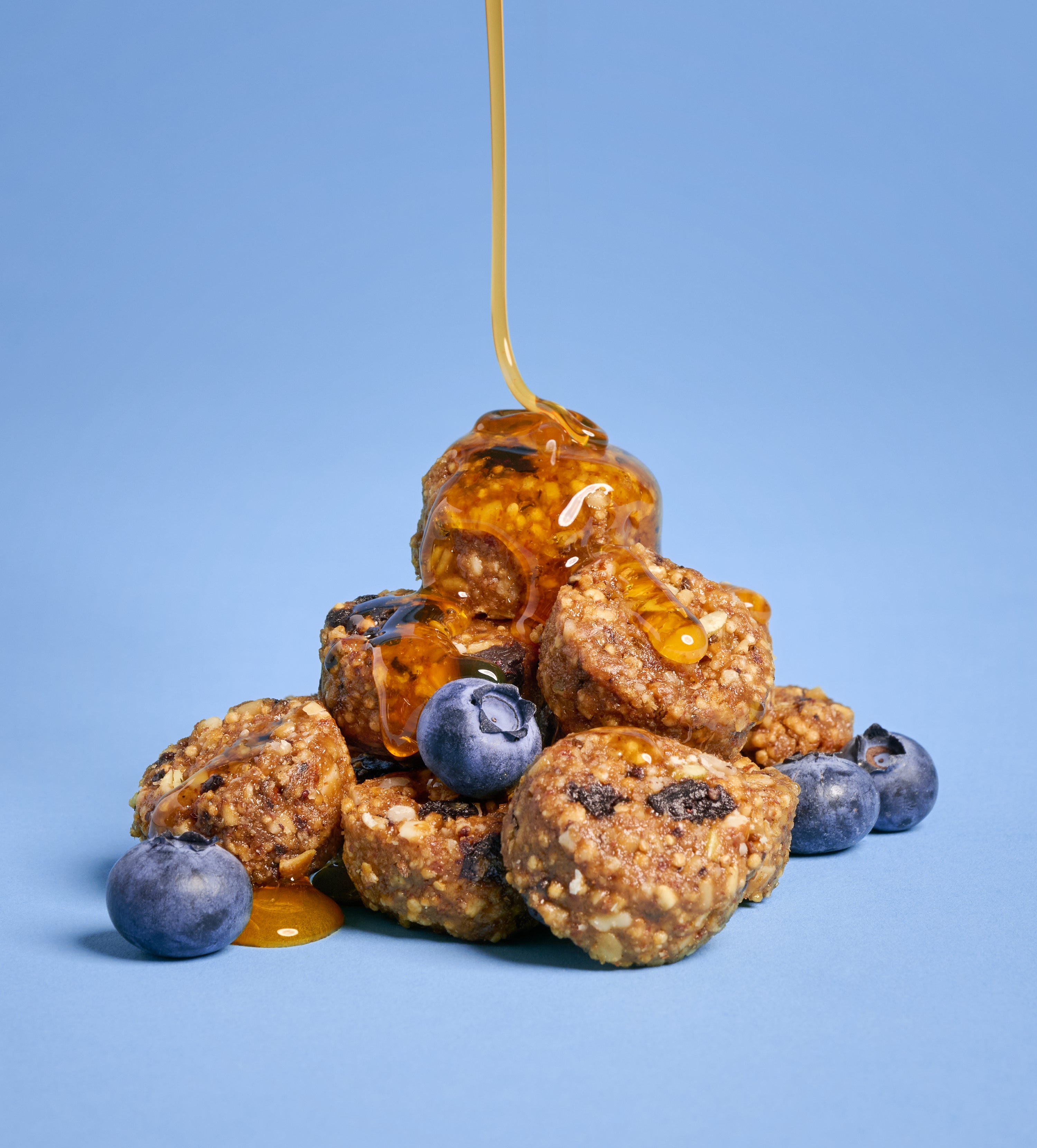 Stacked blueberry honey almond granola bites with sticky honey drizzle against a blue background