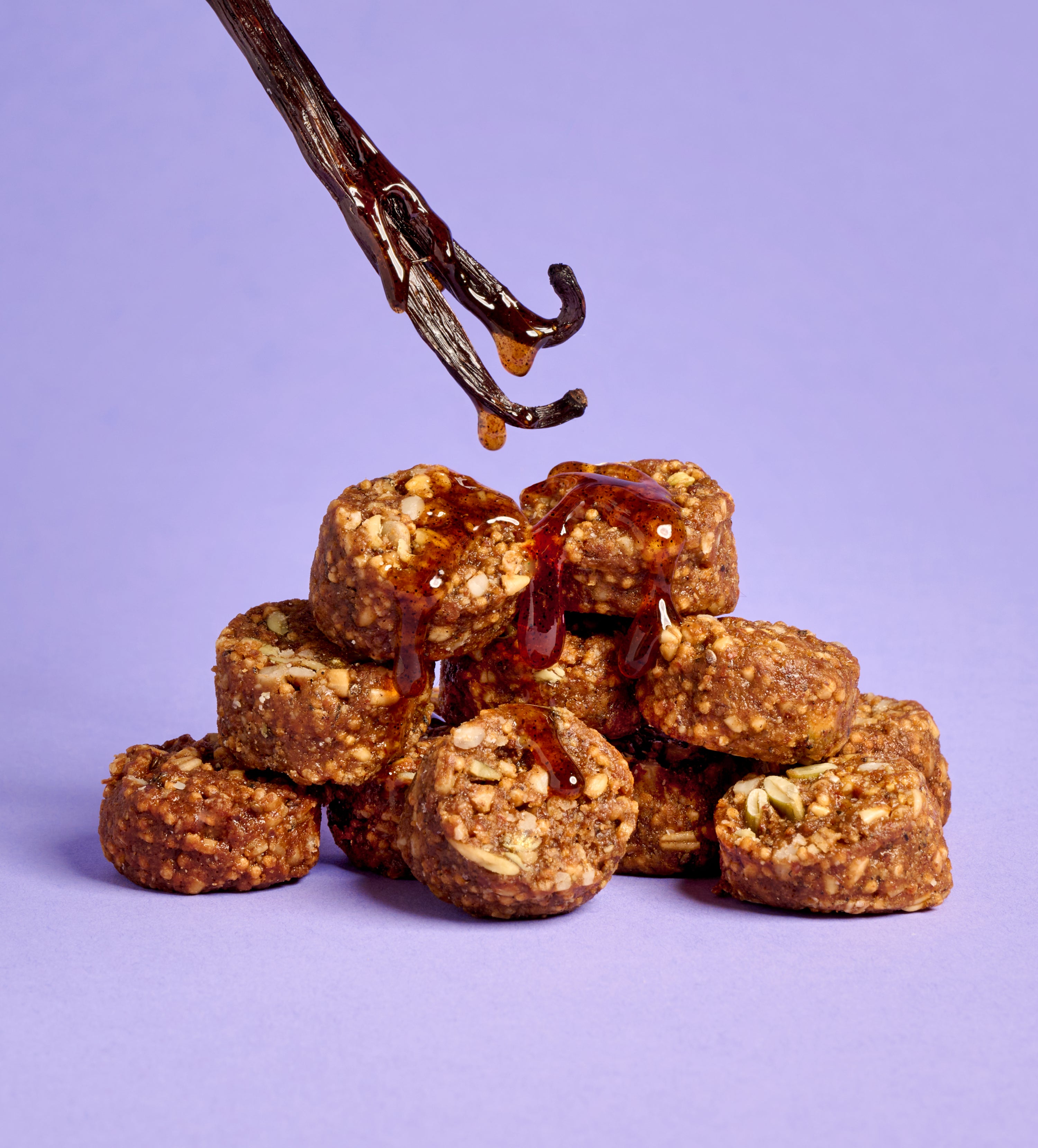Close up of granola bites with chocolate drizzle and dark chocolate chunks on a pink background