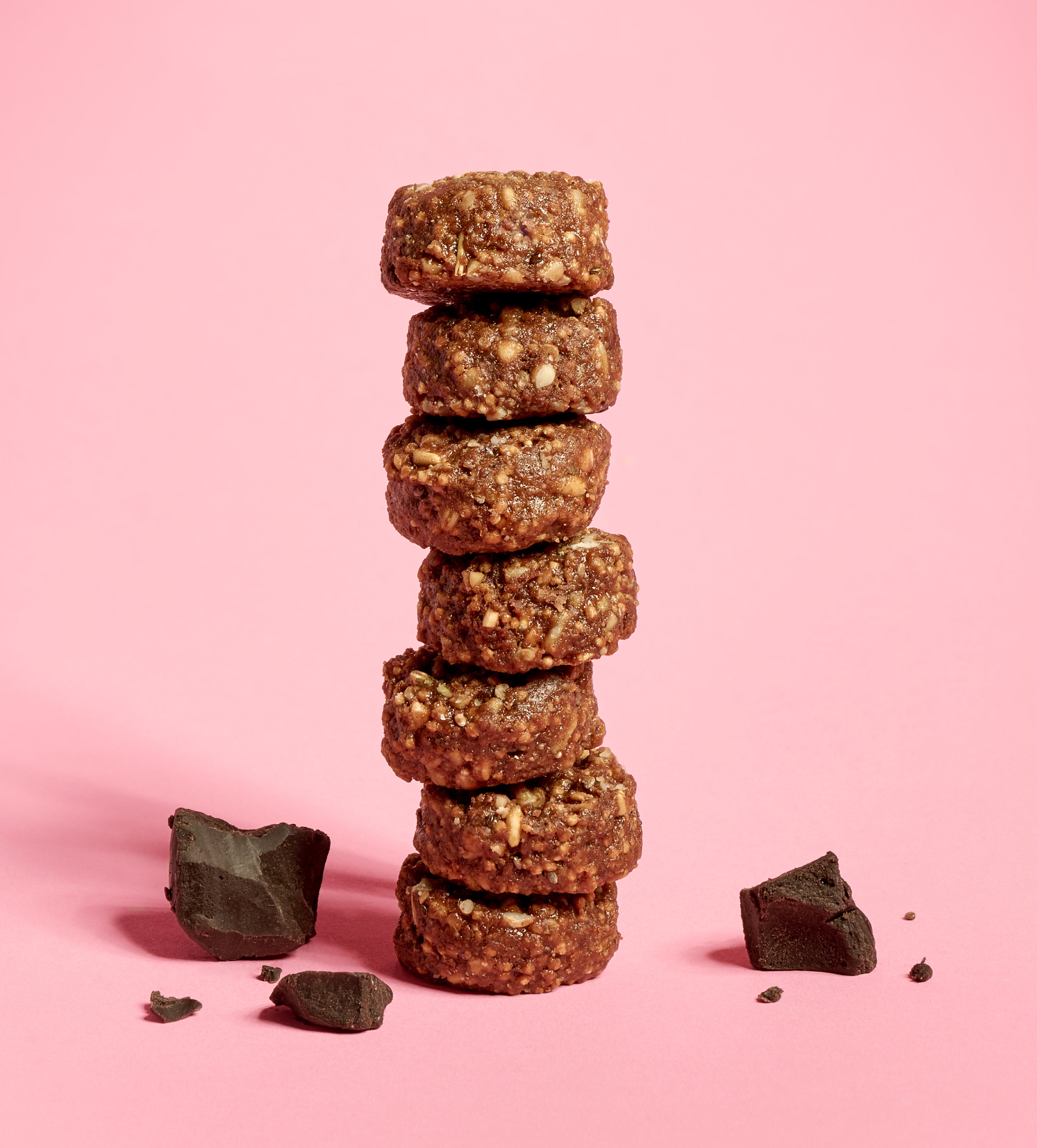 Stack of granola bites studded with nuts on a pink background