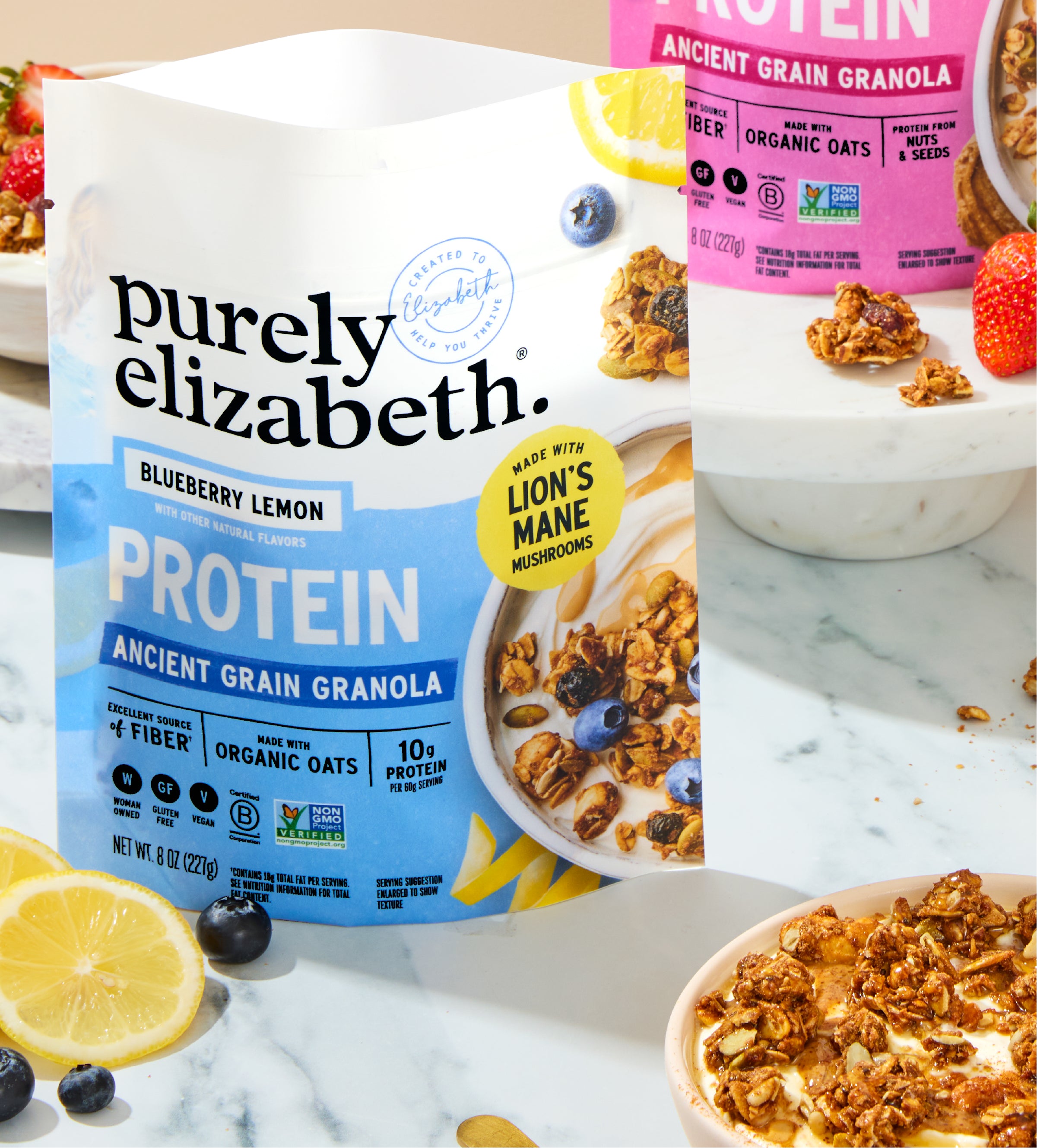 Purely Elizabeth protein granola four pack packaging with a pink bag and fresh fruit nearby