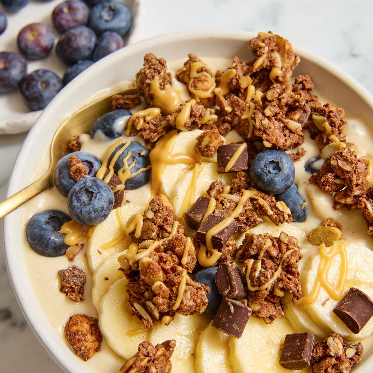 Creamy bowl topped with banana slices blueberries granola clusters and caramel drizzle